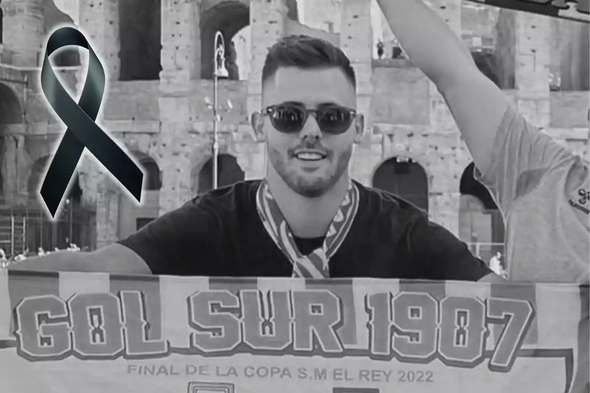Un hombre con gafas de sol sostiene una bufanda que dice "Gol Sur 1907" frente a un edificio antiguo, con un lazo negro superpuesto en la imagen.