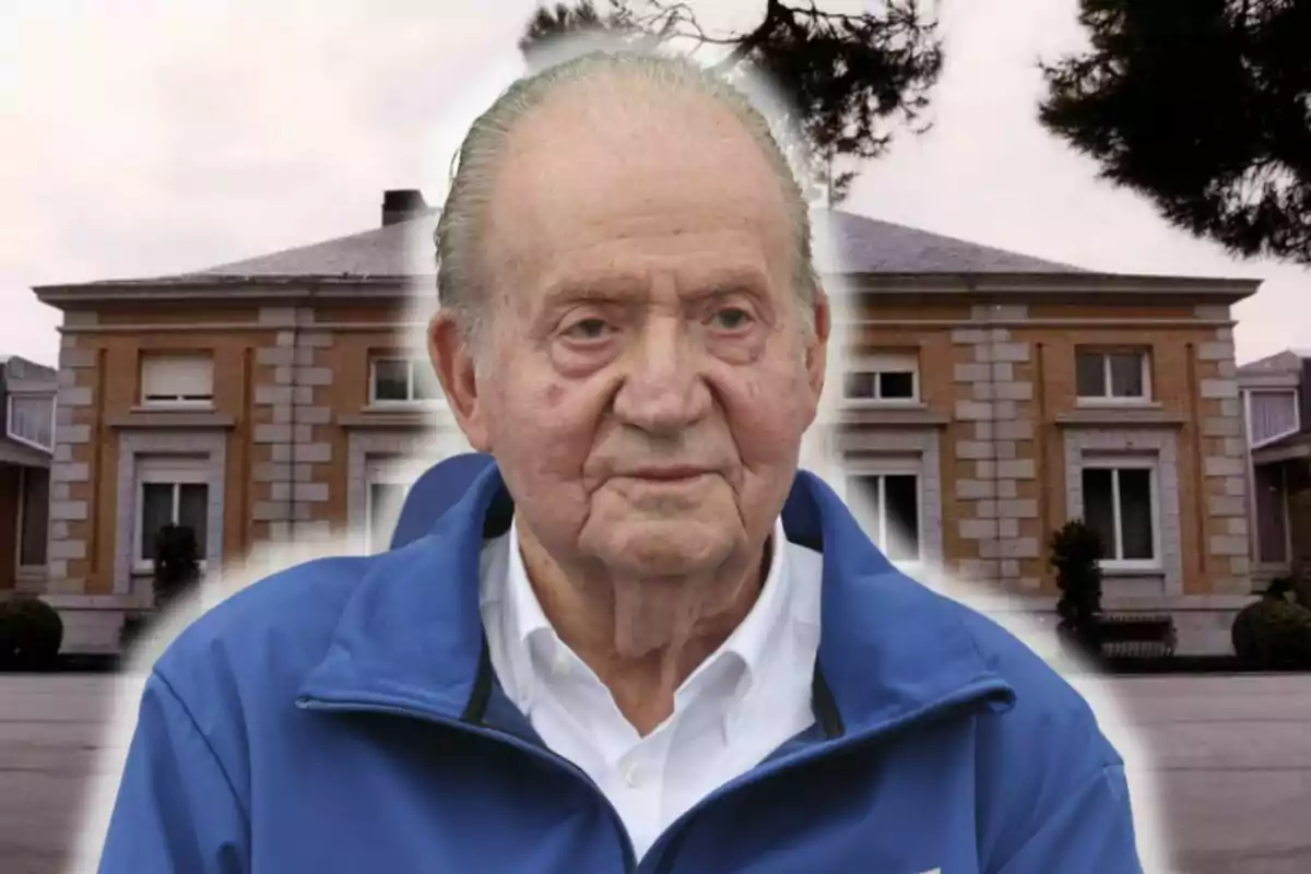 Juan Carlos I con chaqueta azul está frente a un edificio de ladrillo con ventanas y árboles alrededor.