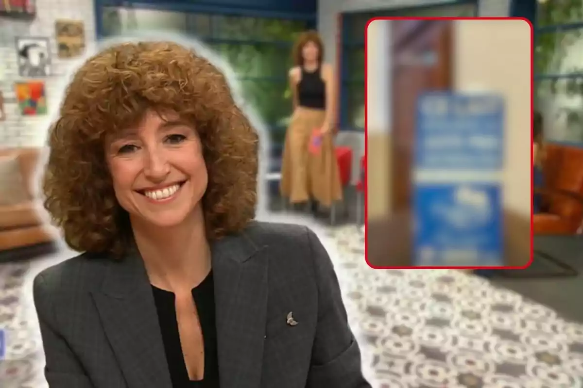 Agnès Marquès sonriente con cabello rizado y un traje gris oscuro, en un entorno interior con decoración moderna y una persona desenfocada en el fondo.