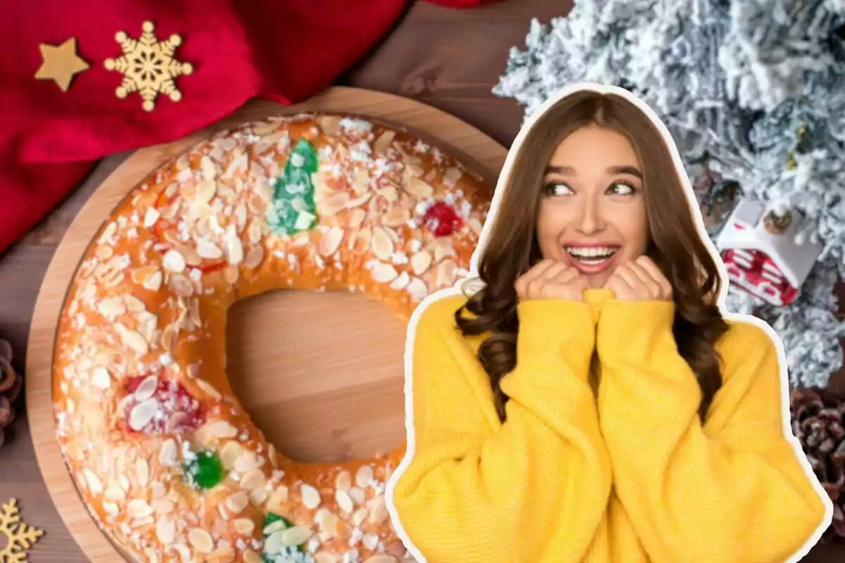 Una mujer sonriente con un suéter amarillo está al lado de un roscón de Reyes decorado con frutas confitadas y almendras, sobre una mesa con adornos navideños.