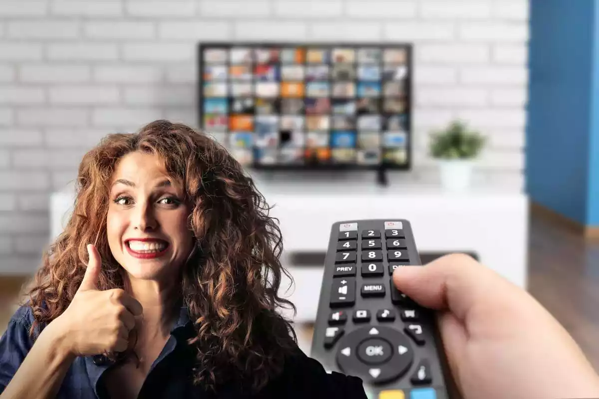 Una persona con un mando a distancia y un televisor al fondo, mientras que a la izquierda una mujer levanta el pulgar sonriente