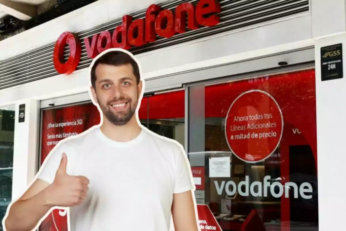 Un hombre sonriente con una camiseta blanca y el pulgar hacia arriba está frente a una tienda de Vodafone.