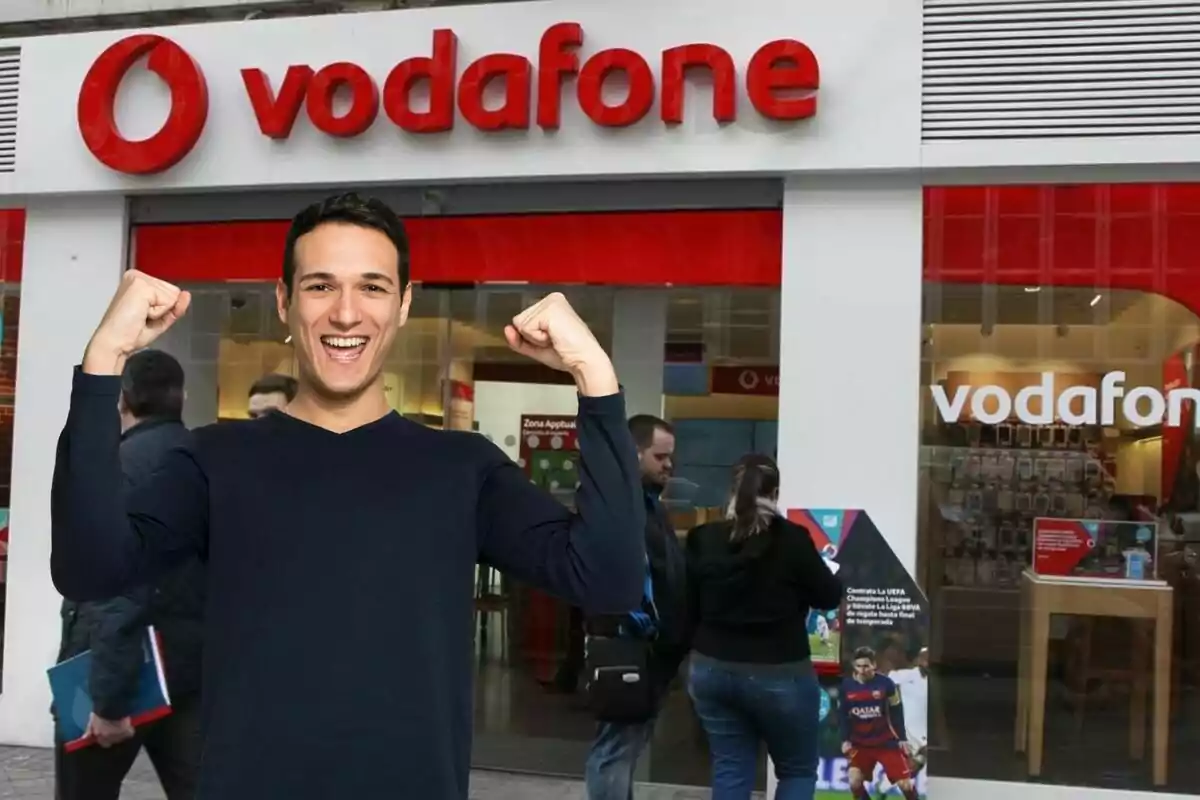 Un hombre sonriente con los brazos levantados frente a una tienda de Vodafone.