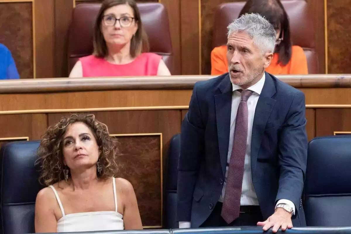 Plano medio de Fernando Grande-Marlaska hablando desde su asiento en el Congreso de los Diputados al lado de María Jesús Montero, que mira al techo