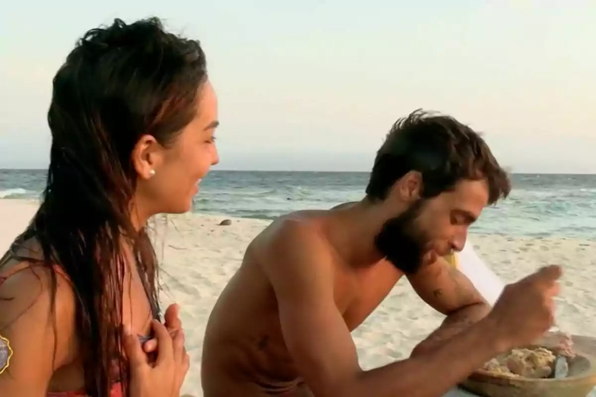 Anita y Montoya en la playa, una mujer sonríe mientras un hombre come de un plato, con el mar de fondo en 'Supervivientes'. Anita y Montoya en la playa, una mujer sonríe mientras un hombre come de un plato, con el mar de fondo en 'Supervivientes'.