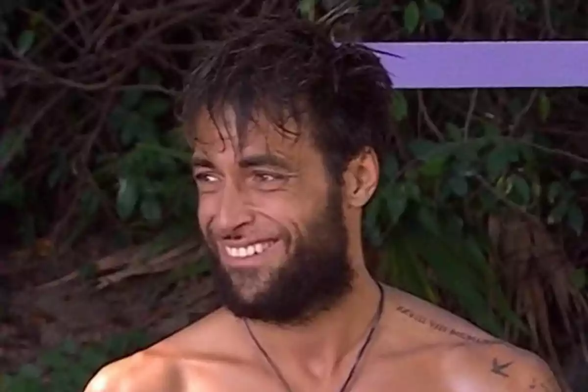 Montoya con barba y cabello despeinado sonríe al aire libre con vegetación de fondo en Supervivientes.