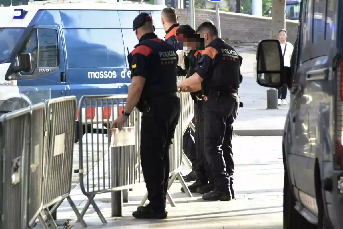 Policías colocando vallas de seguridad en una calle mientras una furgoneta de la policía está estacionada cerca.