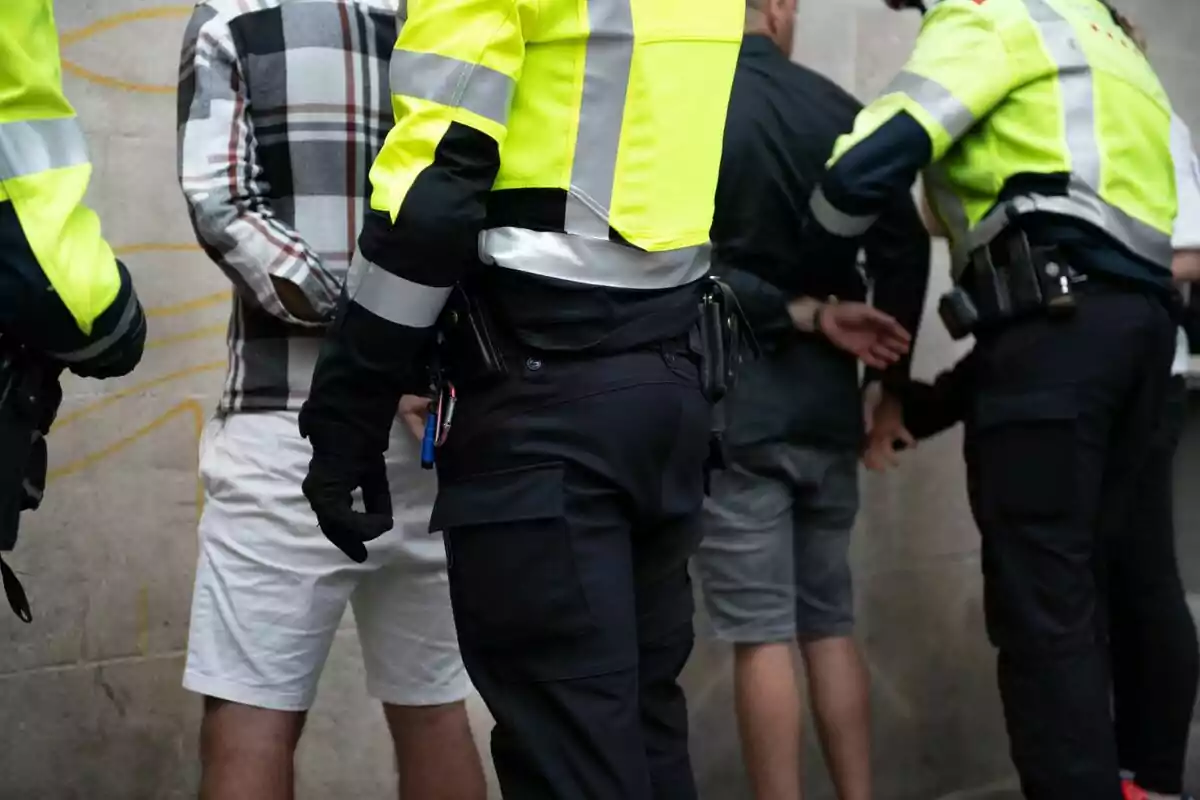 Policías deteniendo a dos personas contra una pared.