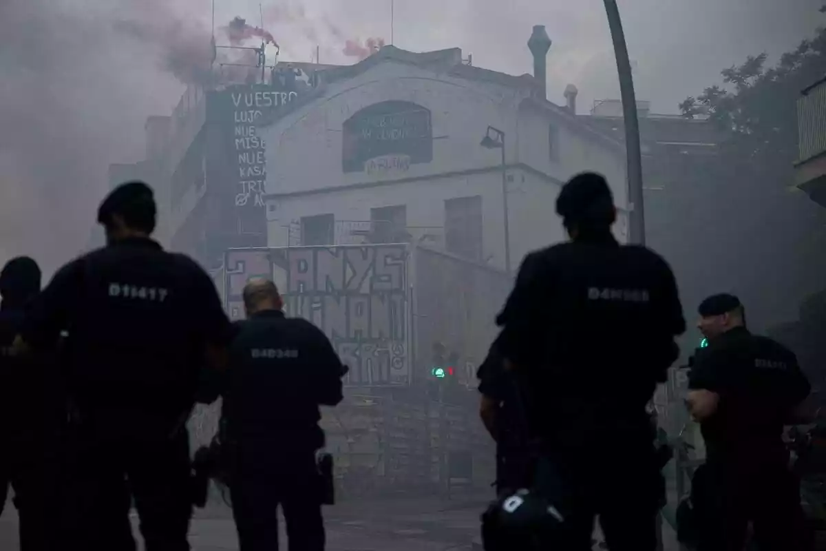 Varios Mossos de espaldas mirando hacia las casas okupadas La Ruïna y Kubo de la Bonanova con mucho humo en el aire