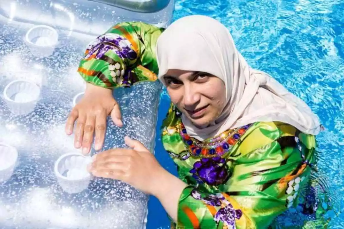 Imagen de una mujer con burkini en una piscina sujetada a una colchoneta