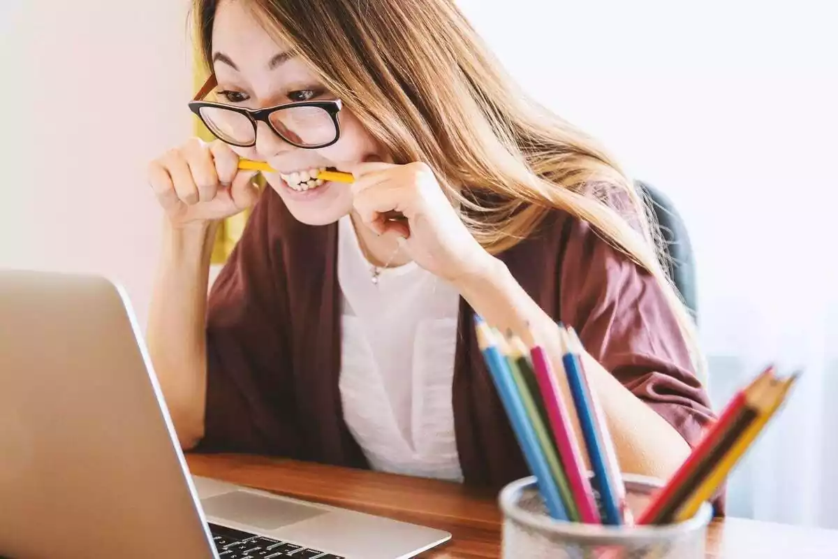 Una mujer frente a un ordenador portátil muy nerviosa y con un lápiz en la boca