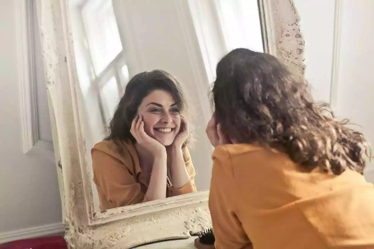 Mujer con pelo castaño mirándose al espejo mientras sonríe felizmente