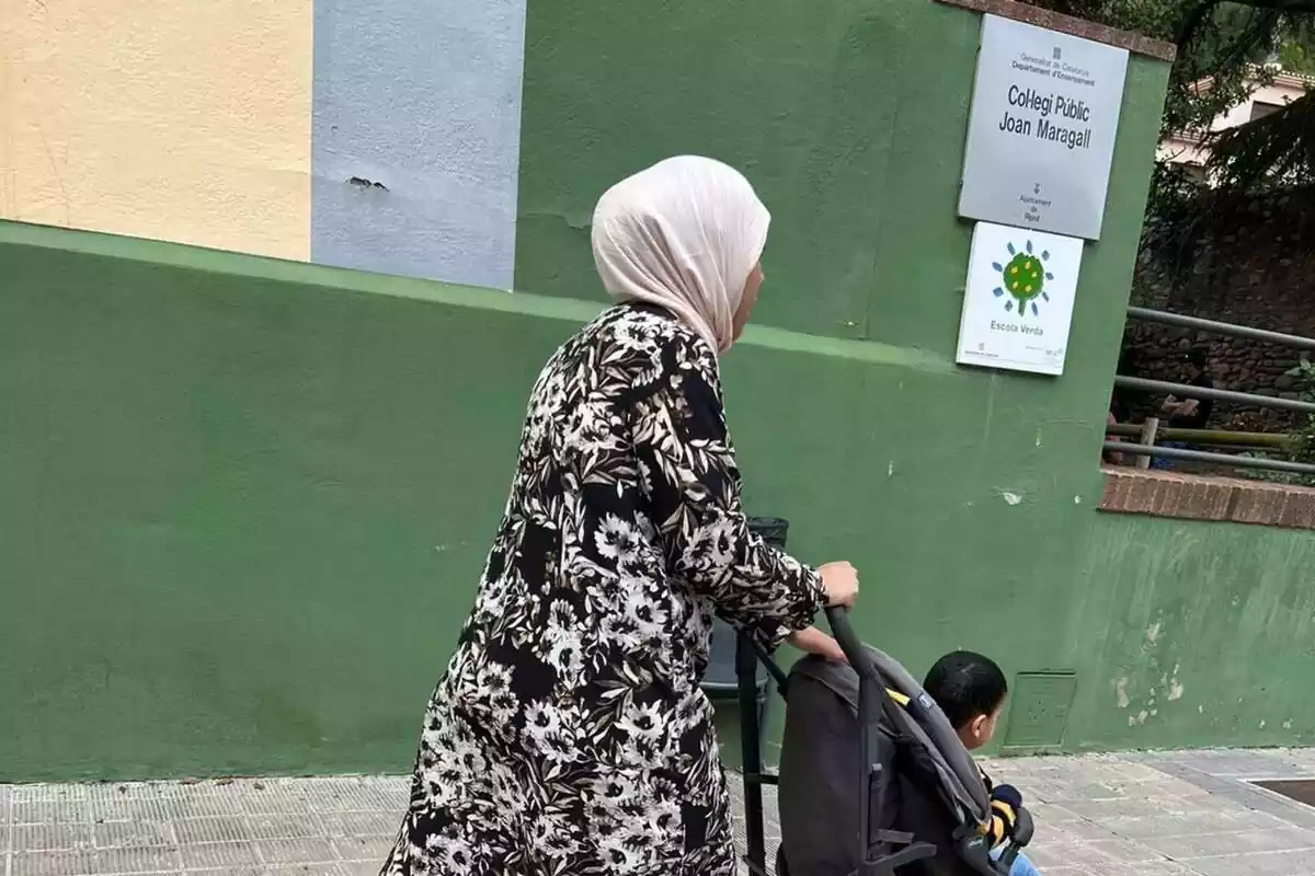 Una mujer musulmana paseando un carrito con un niño delante de una escuela de Ripoll