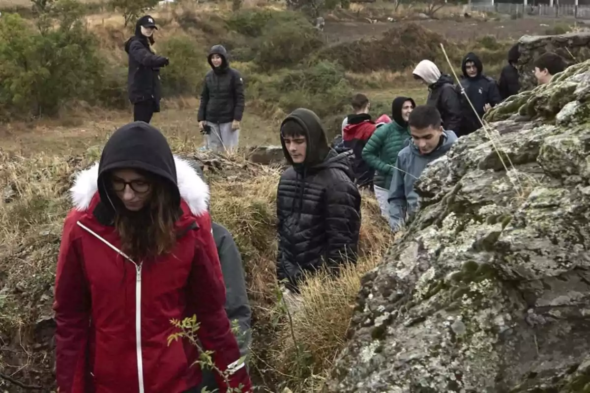 Un grupo de personas con ropa de abrigo camina por un sendero en un entorno natural, rodeado de vegetación y rocas.