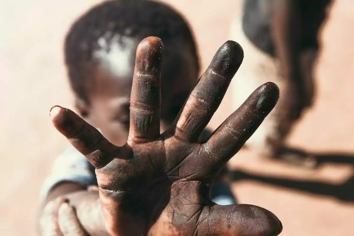 Una mano extendida de un niño cubre parcialmente su rostro en un entorno al aire libre.
