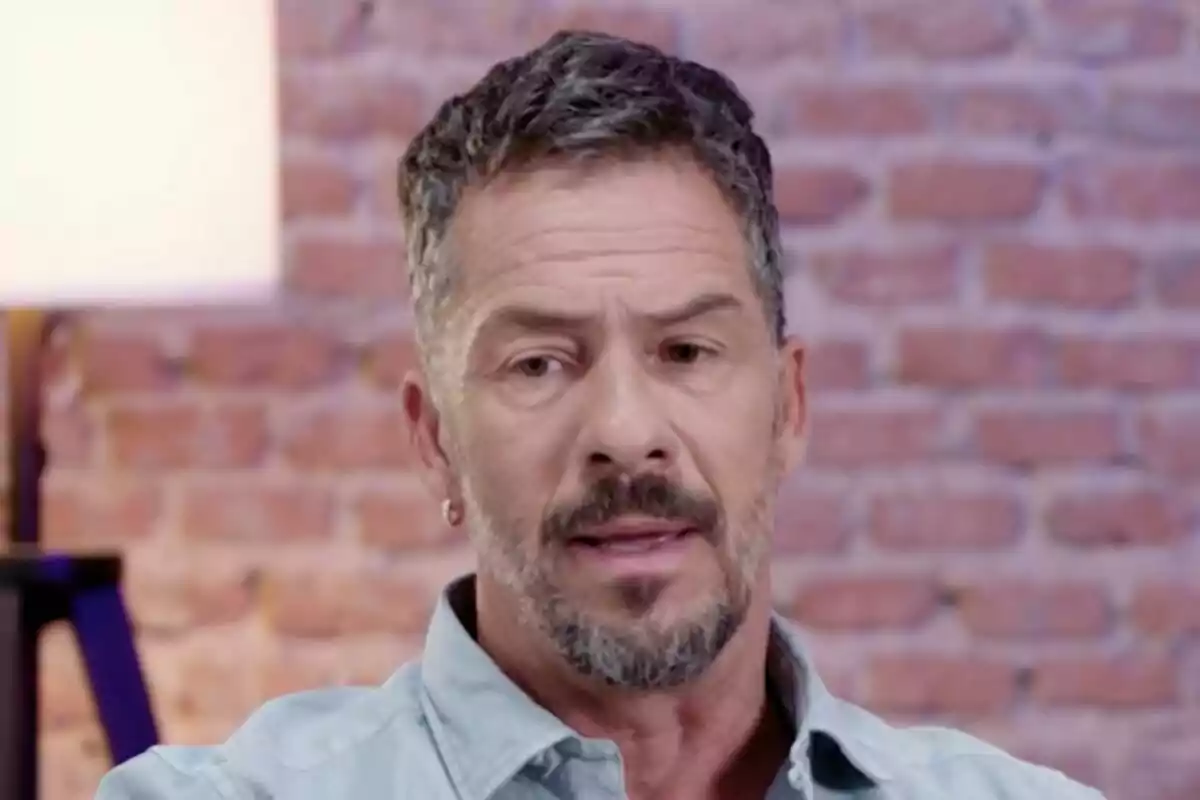 Captura de Nacho Palau con barba y cabello corto canoso, con una expresión seria, frente a una pared de ladrillos en un scoop de De Viernes