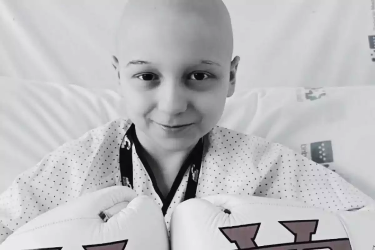 Un niño sonriente con guantes de boxeo blancos en una cama de hospital.