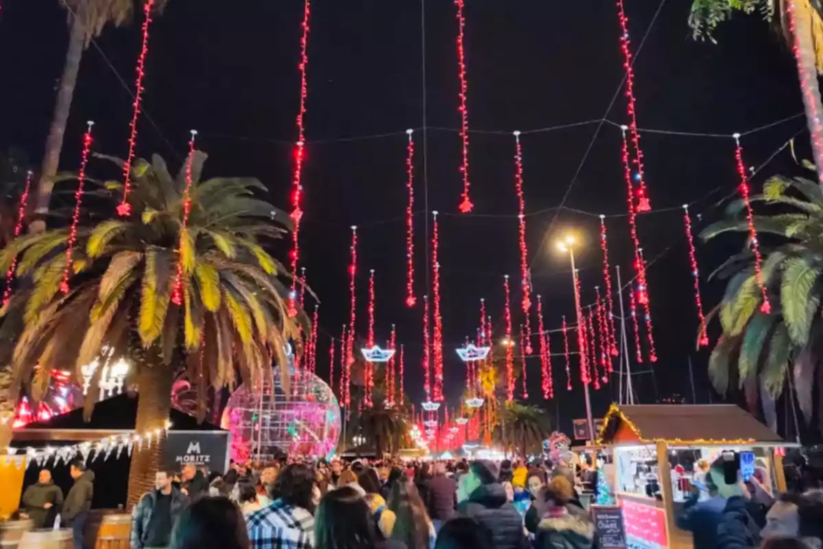 Una multitud disfruta de un mercado nocturno decorado con luces rojas colgantes y palmeras iluminadas.