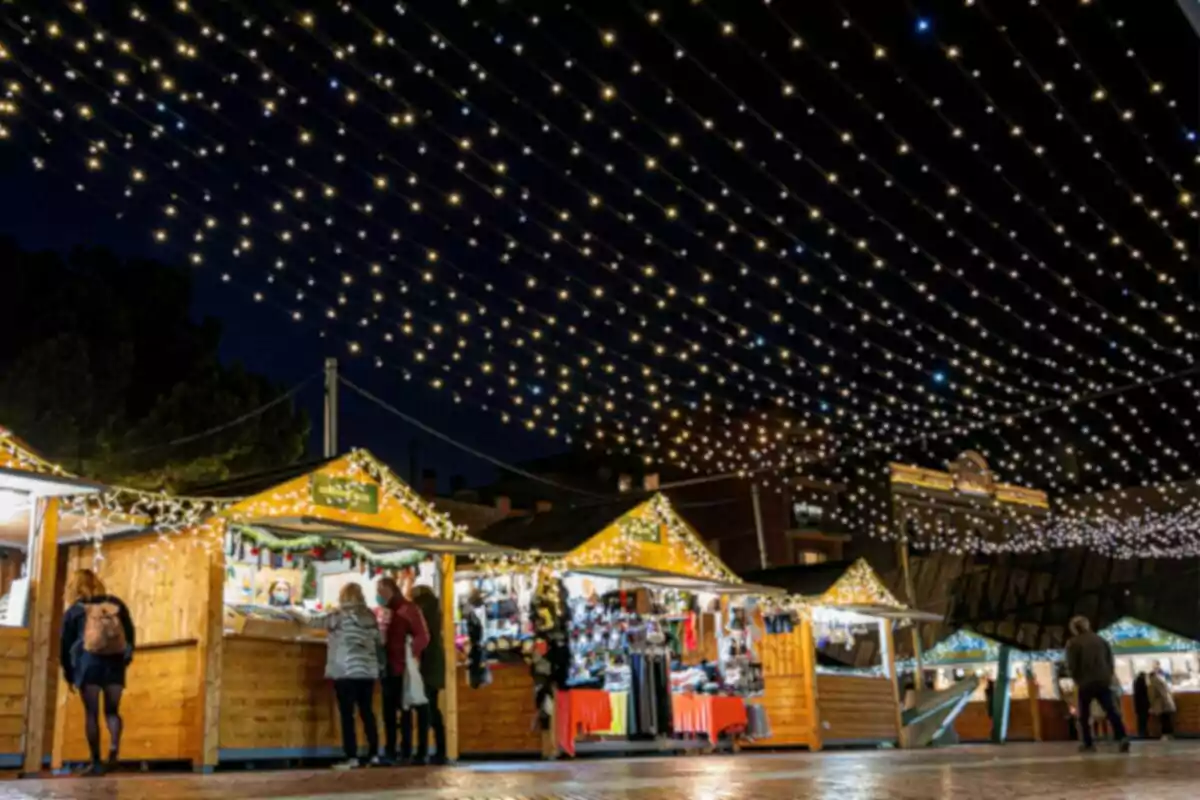 Mercado navideño al aire libre con luces brillantes y puestos de madera iluminados por la noche.