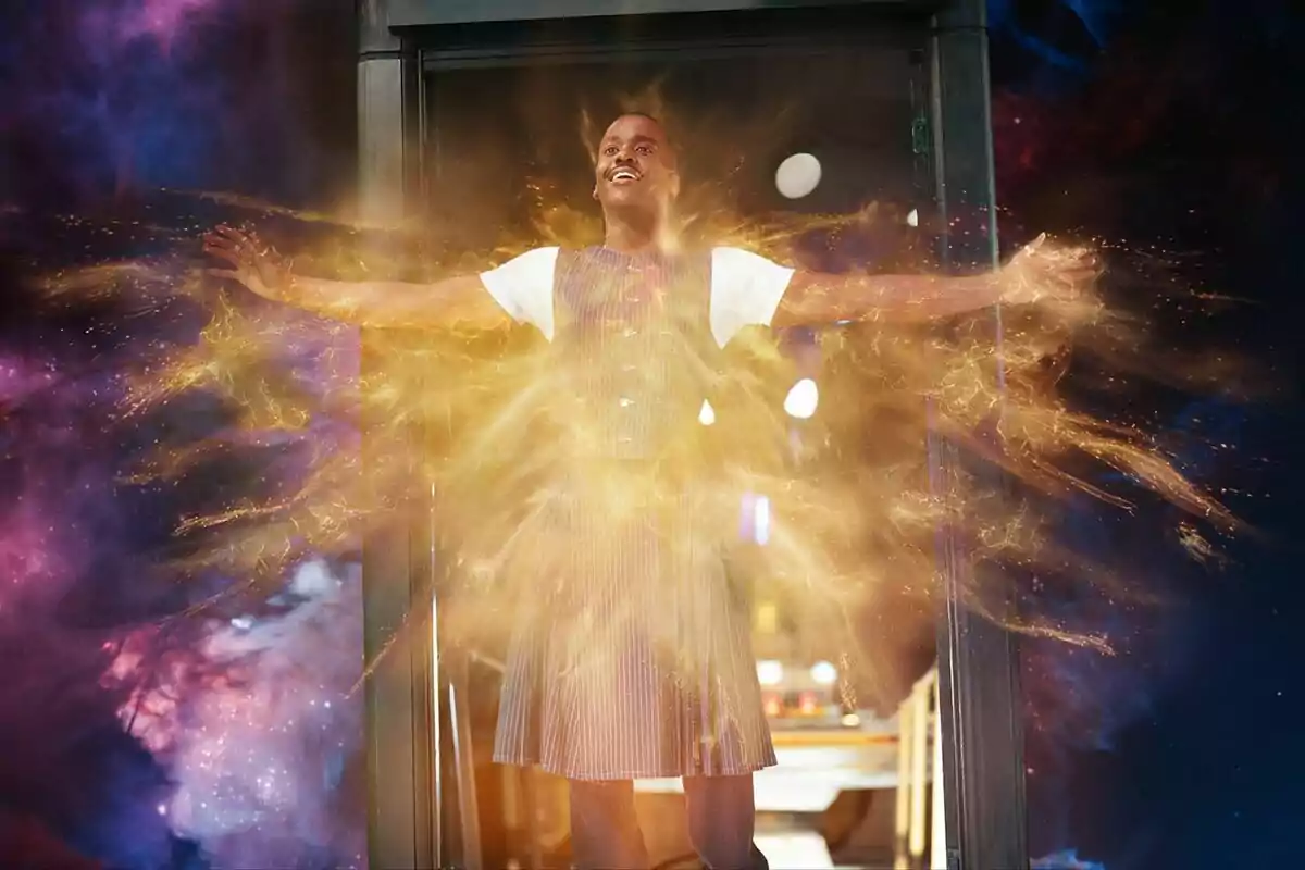 Ncuti Gatwa de pie con los brazos extendidos rodeada de un resplandor dorado y un fondo cósmico colorido en Doctor Who Ncuti Gatwa de pie con los brazos extendidos rodeada de un resplandor dorado y un fondo cósmico colorido en Doctor Who