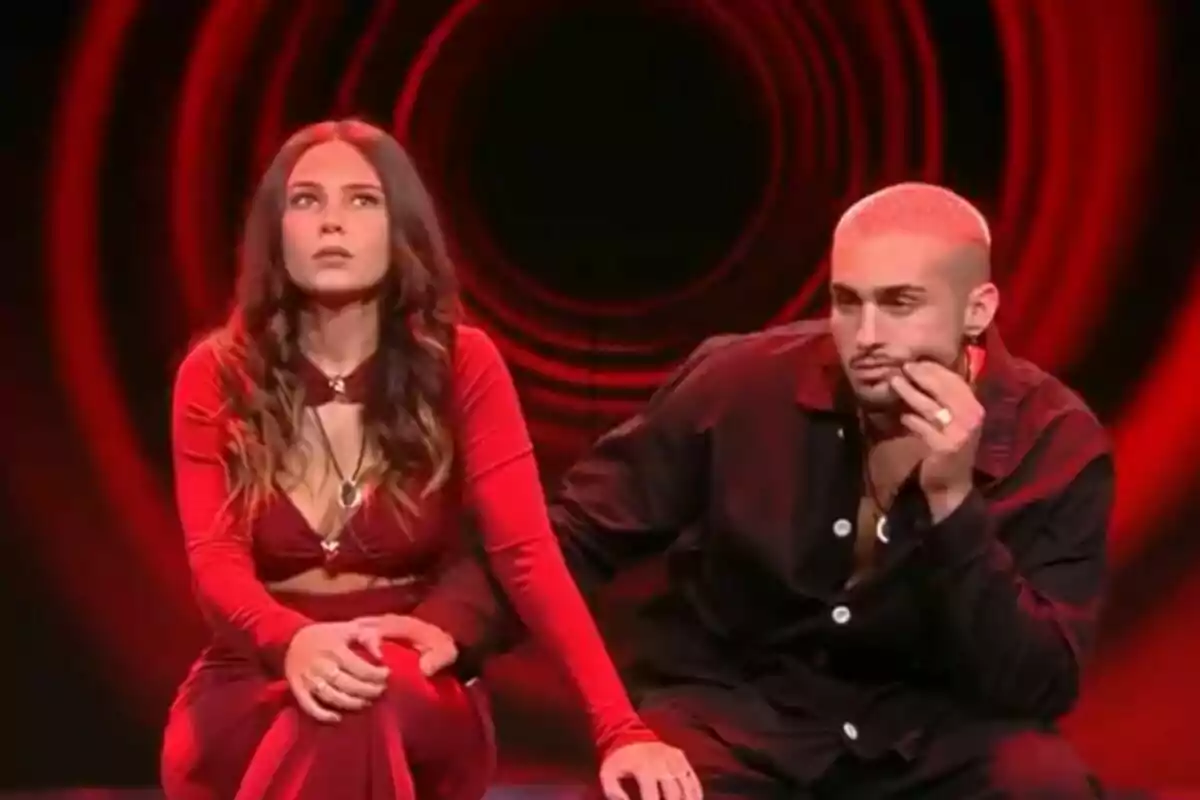 Laura y Manu sentados en la sala de expulsión de Gran Hermano con fondo rojo y negro.