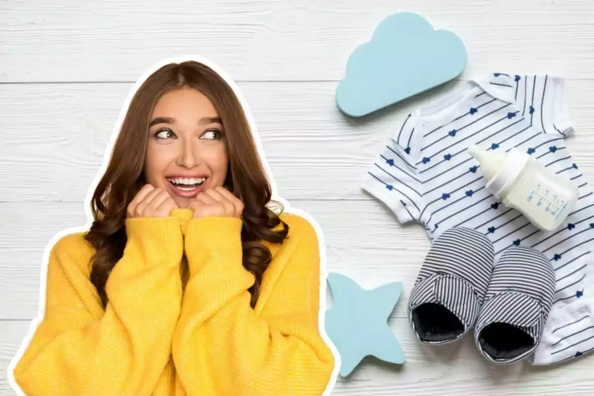 Mujer sonriente con suéter amarillo junto a ropa y accesorios de bebé sobre fondo de madera blanca.