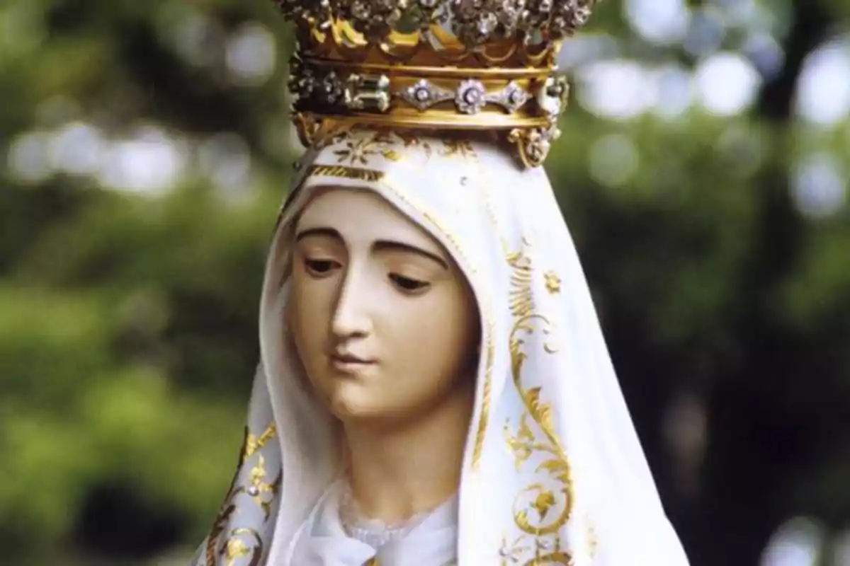 Una estatua de una figura religiosa con una corona dorada y un manto blanco decorado con detalles dorados.