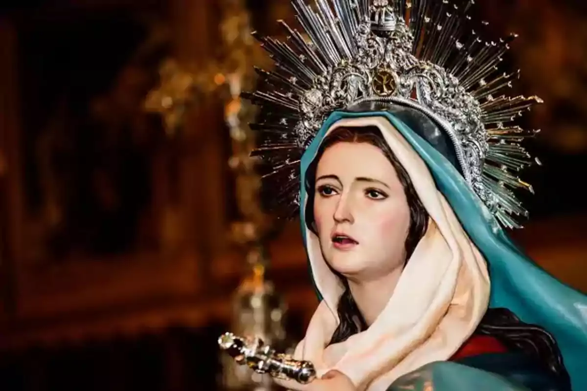 Imagen de una escultura religiosa de la Virgen María con manto azul y corona plateada decorada con rayos, en un entorno de iglesia. Imagen de una escultura religiosa de la Virgen María con manto azul y corona plateada decorada con rayos, en un entorno de iglesia.