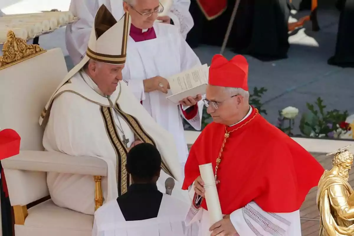 Un líder religioso sentado en una ceremonia mientras interactúa con un cardenal que sostiene un documento, acompañado por asistentes en vestimenta litúrgica. Un líder religioso sentado en una ceremonia mientras interactúa con un cardenal que sostiene un documento, acompañado por asistentes en vestimenta litúrgica.