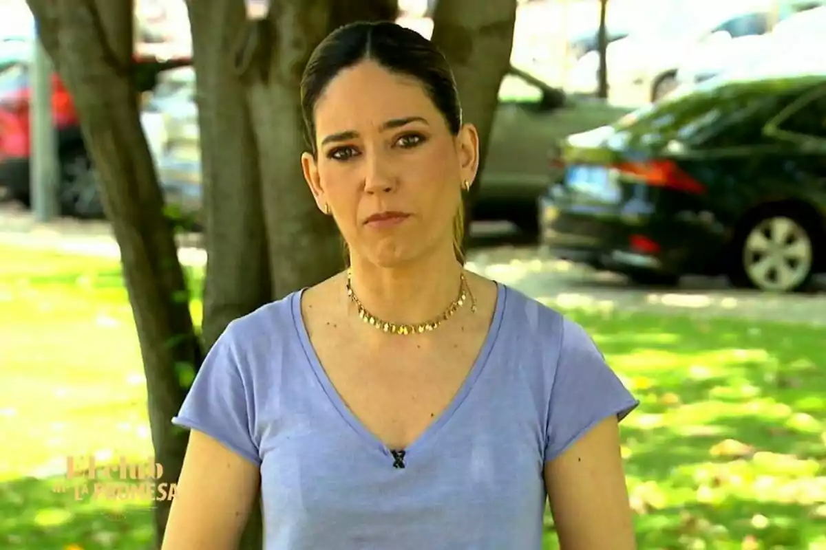 Nuria Martín de cabello oscuro recogido y camiseta lila de pie al aire libre con expresión seria, árboles y autos desenfocados al fondo en El Club de La Promesa Nuria Martín de cabello oscuro recogido y camiseta lila de pie al aire libre con expresión seria, árboles y autos desenfocados al fondo en El Club de La Promesa