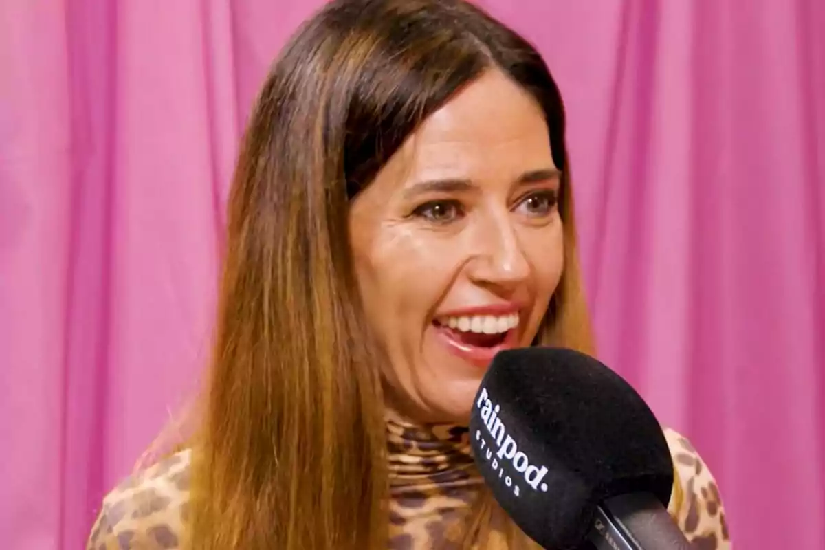 Nuria Marín sonriendo mientras habla frente a un micrófono con fondo rosa.