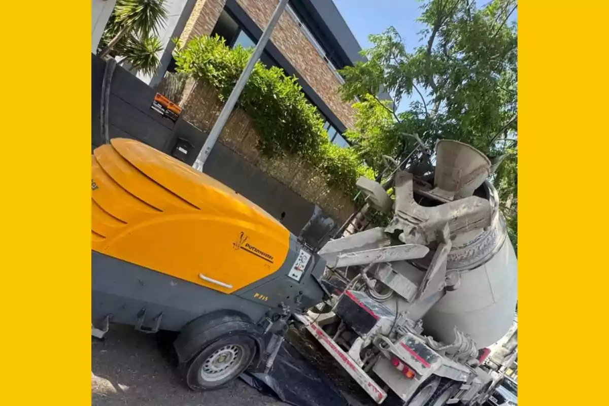 Máquina amarilla conectada a una revolvedora de cemento frente a una casa moderna con árboles y vegetación Máquina amarilla conectada a una revolvedora de cemento frente a una casa moderna con árboles y vegetación