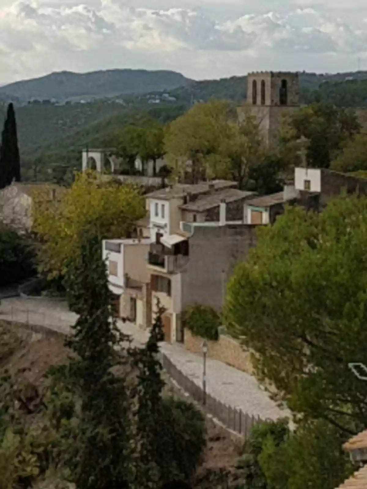 Una vista panorámica de un pequeño pueblo con casas de piedra y una torre antigua rodeada de colinas verdes y árboles. Una vista panorámica de un pequeño pueblo con casas de piedra y una torre antigua rodeada de colinas verdes y árboles.