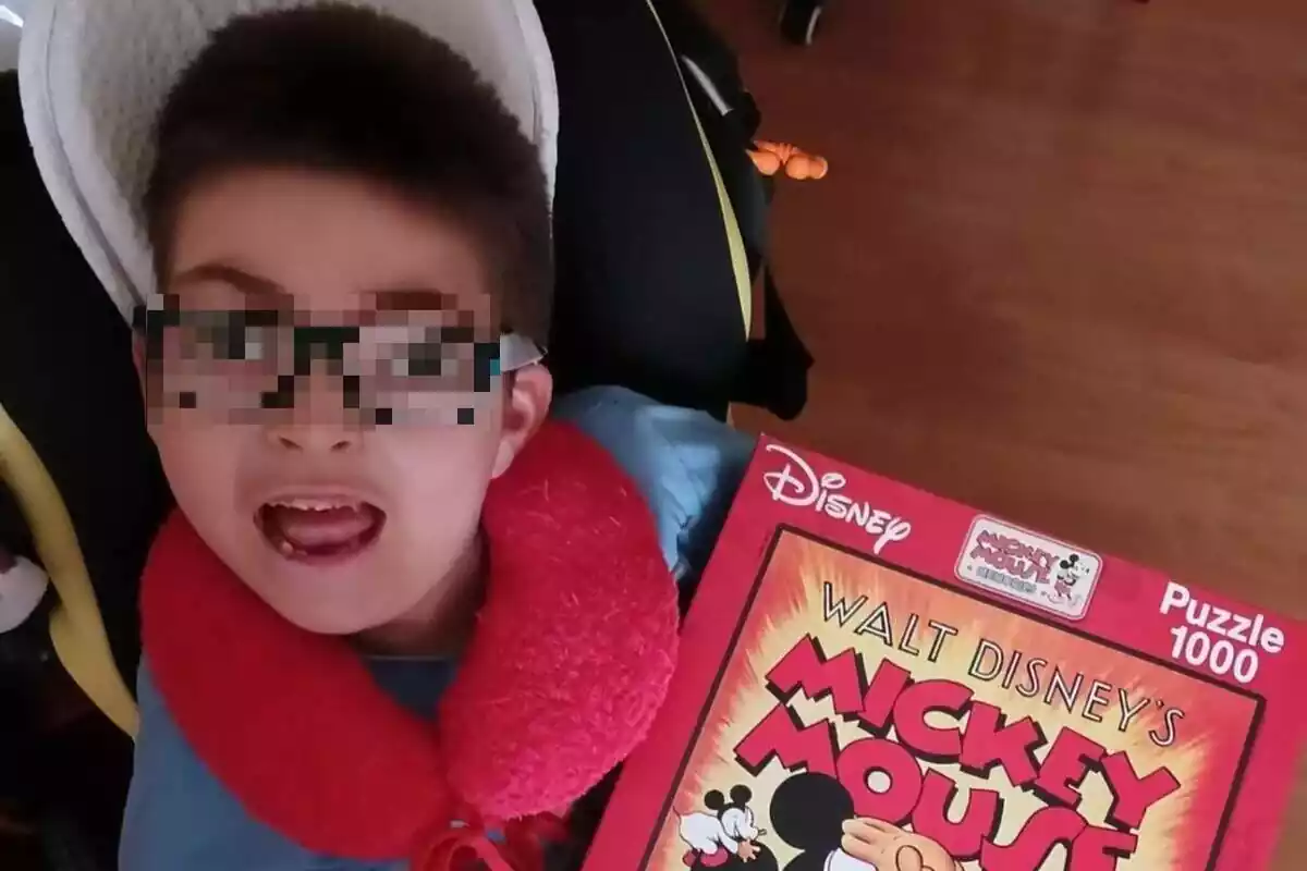 Plano corto de Oliver, un niño que padece Síndrome de West, con rostro sonriente, y un libro de Mickey Mouse en la mano