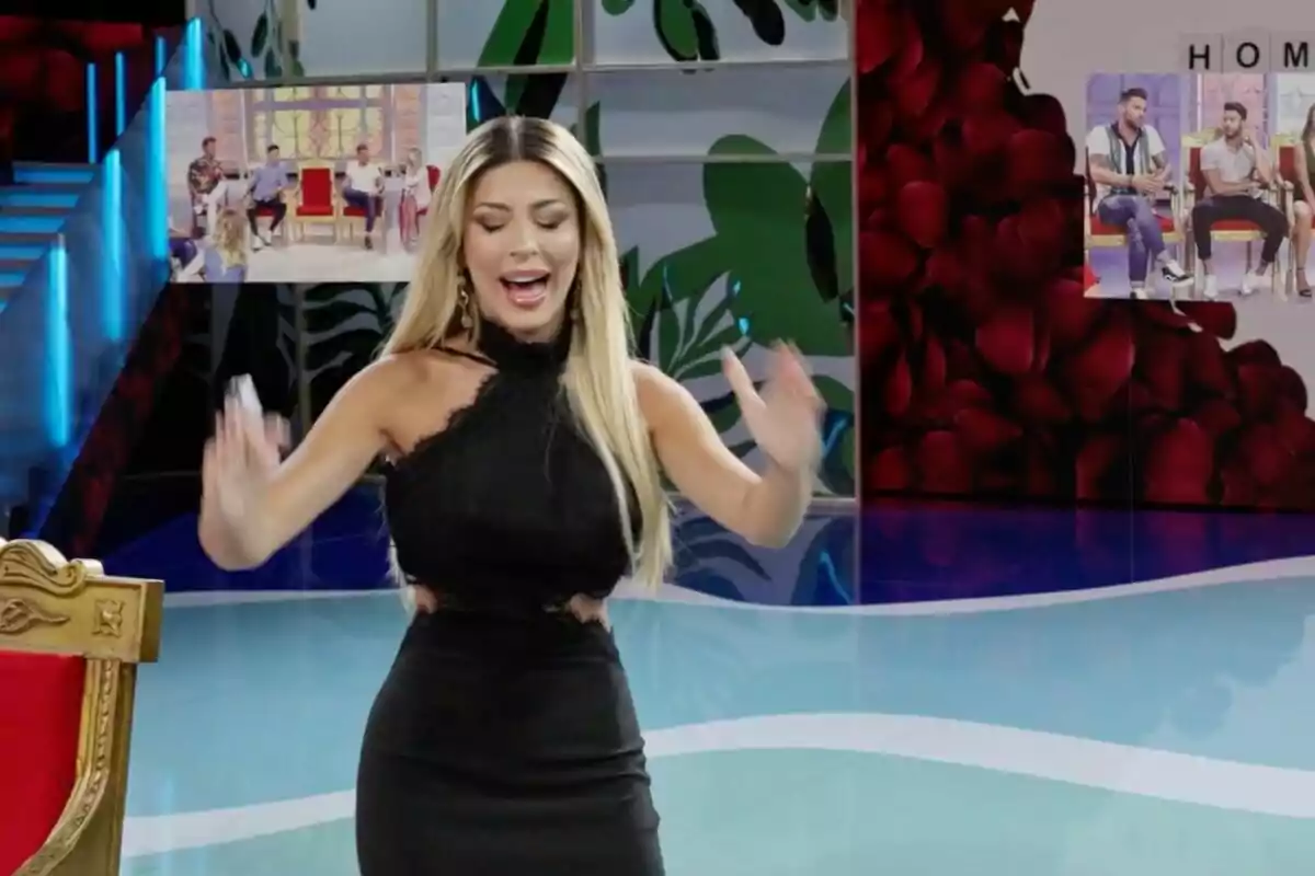 Oriana Marzoli con vestido negro está gesticulando en un set de televisión colorido, con pantallas al fondo mostrando a varias personas sentadas. Oriana Marzoli con vestido negro está gesticulando en un set de televisión colorido, con pantallas al fondo mostrando a varias personas sentadas.