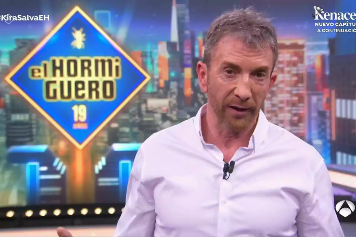 Pablo Motos con camisa blanca está hablando en un programa de televisión llamado "El Hormiguero" con un fondo colorido y urbano.