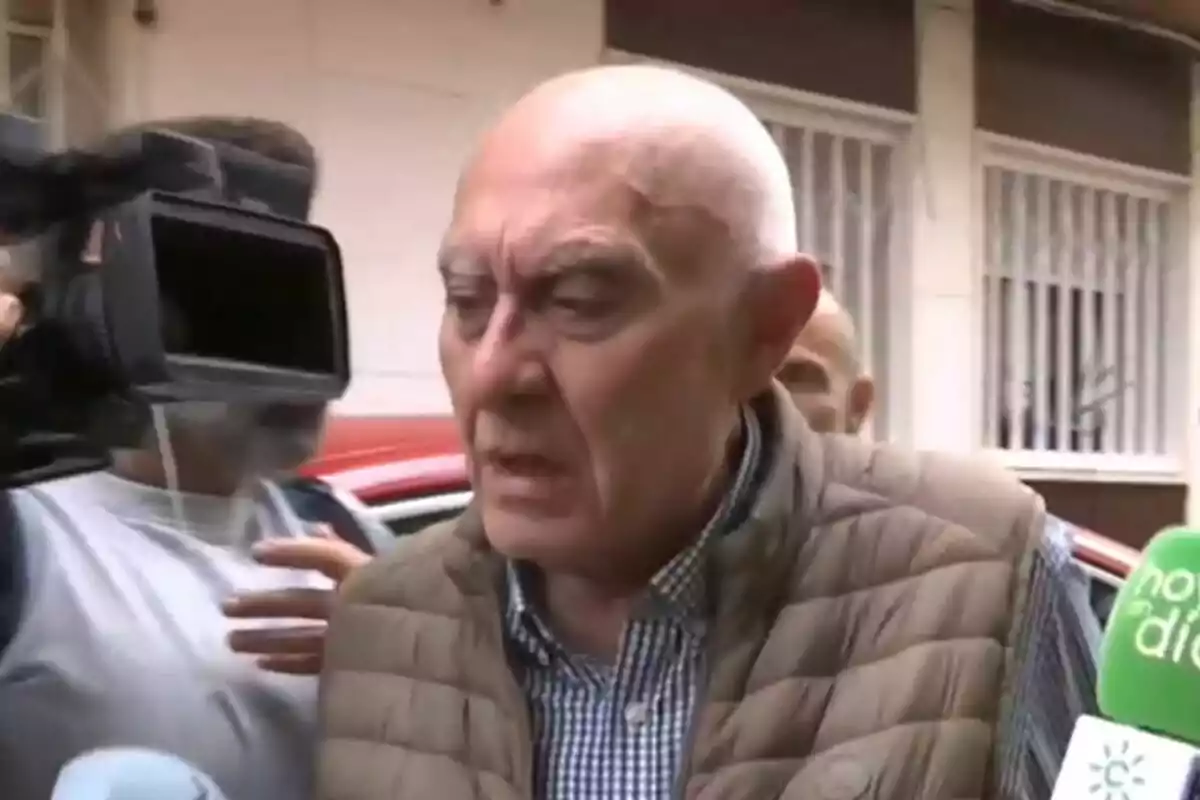 Un hombre mayor con chaleco marrón es entrevistado por varios medios de comunicación en la calle. Un hombre mayor con chaleco marrón es entrevistado por varios medios de comunicación en la calle.