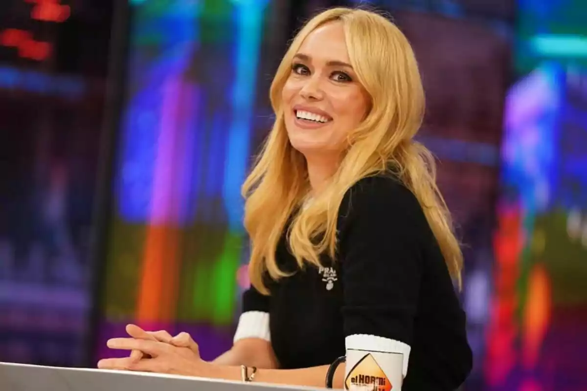 Patricia Conde rubia sonriendo sentada en 'El Hormiguero' con fondo colorido y una taza de 'El Hormiguero' sobre la mesa
