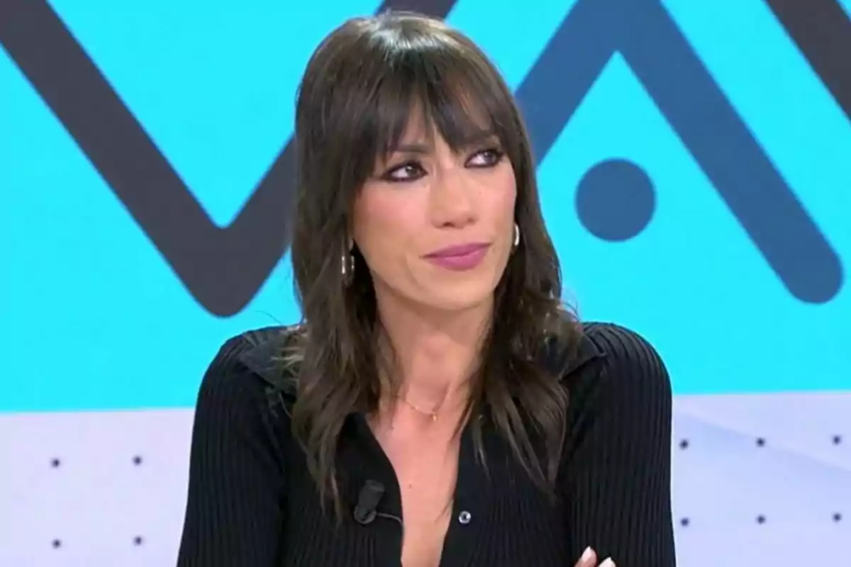 Patricia Pardo con cabello oscuro y flequillo muy emocionada está sentada frente a un fondo azul con patrones geométricos en el plató de Vamos a ver.