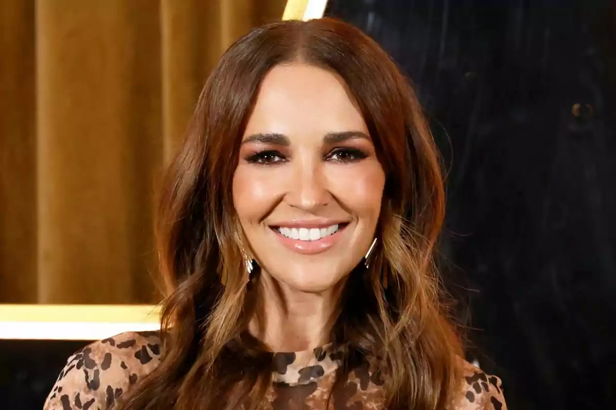 Paula Echevarría sonriendo con cabello largo y suelto, usando un vestido con estampado de leopardo, fondo dorado y negro en la presentación de Got Talent.