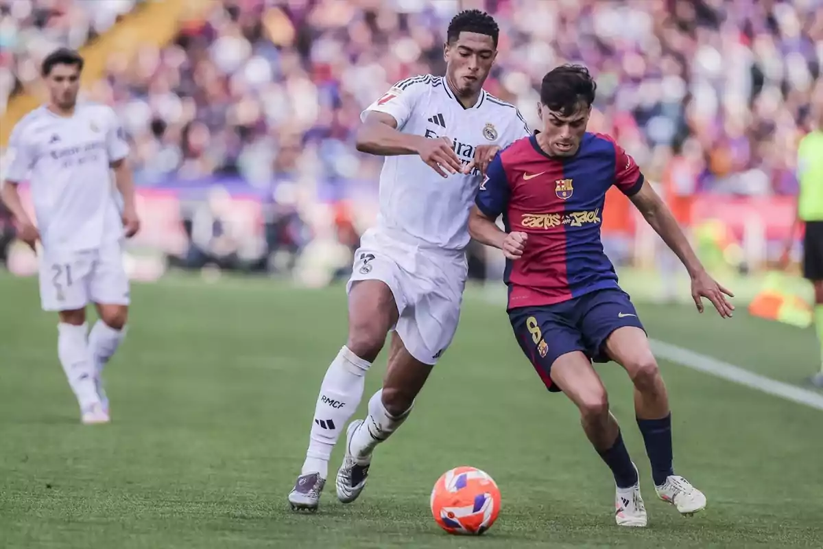 Dos jugadores de fútbol compiten por el balón en un partido, uno viste de blanco y el otro de azul y rojo. Dos jugadores de fútbol compiten por el balón en un partido, uno viste de blanco y el otro de azul y rojo.