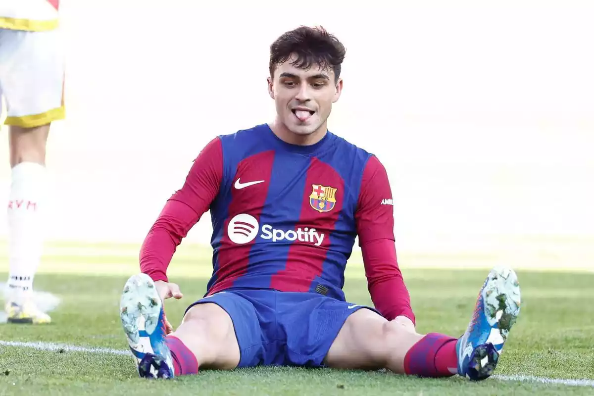 Pedri sentado en el suelo con la lengua fuera mirándose la bota derecha durante un partido del FC Barcelona