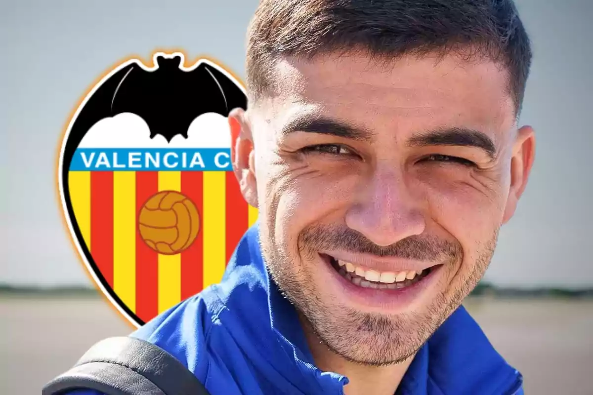 Un hombre sonriente con una chaqueta azul frente al escudo del Valencia CF.