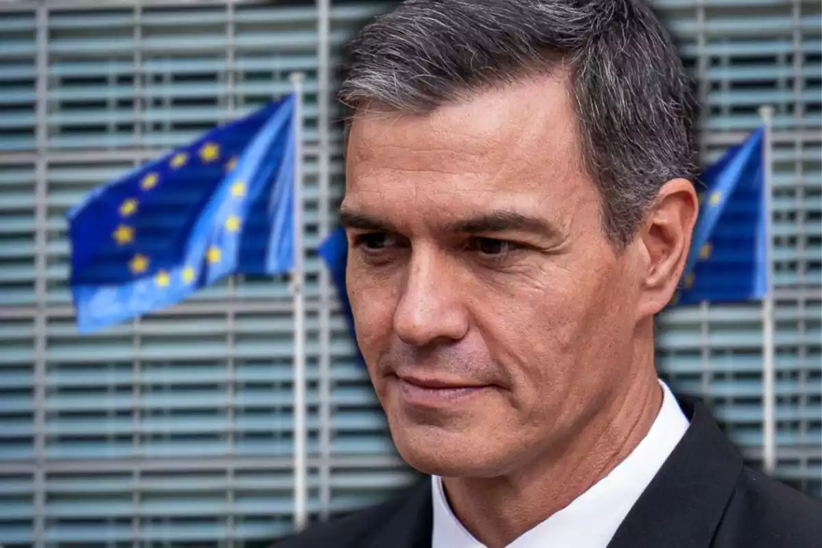 Primer plano de Pedro Sánchez con cara seria mirando hacia el suelo y de fondo una imagen de la fachada de la Comisión Europea y varias banderas de la Unión Europea