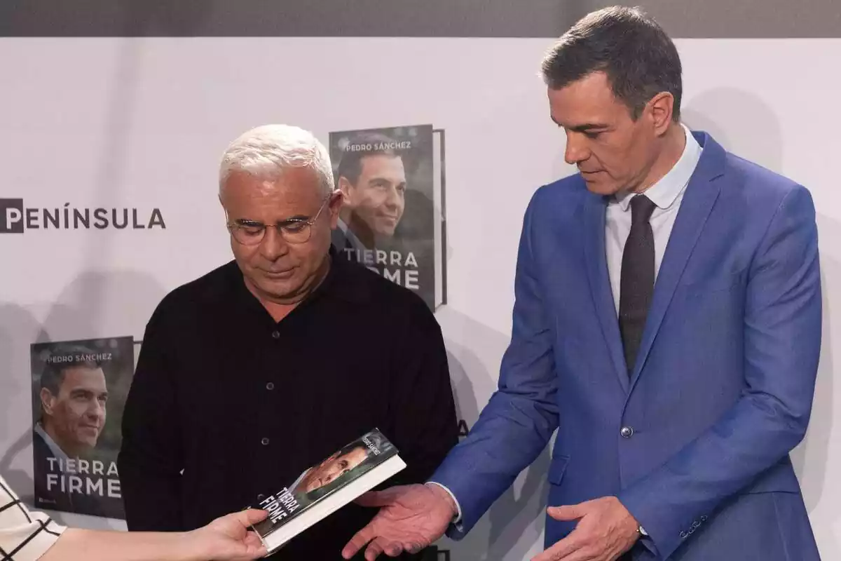 Plano medio de Jorge Javier Vázquez y Pedro Sánchez mirando hacia abajo, donde una mujer les acerca un libro de Pedro Sánchez