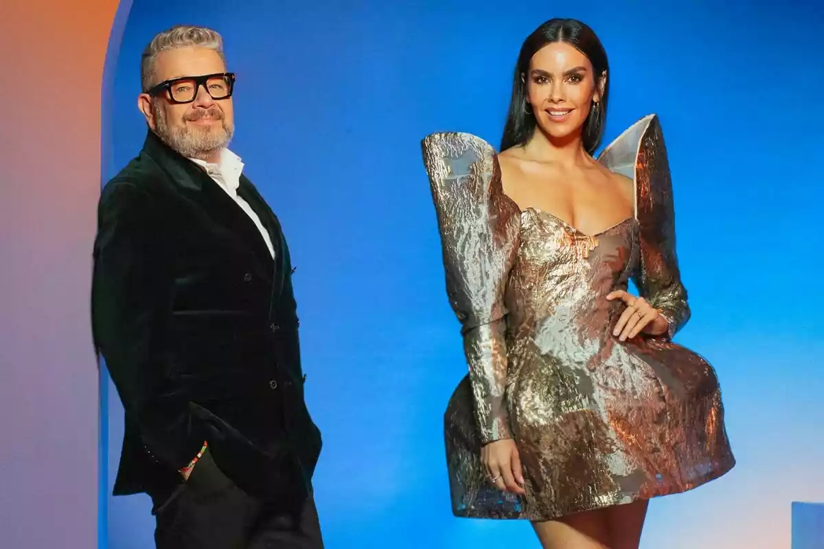 Alberto Chicote y Cristina Pedroche posan frente a un fondo azul, una de ellas lleva un vestido metálico con volúmenes y la otra un traje oscuro con gafas.