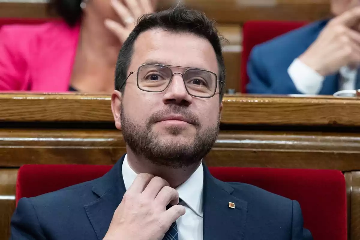 Hombre con gafas y barba en un entorno formal ajustándose la corbata.