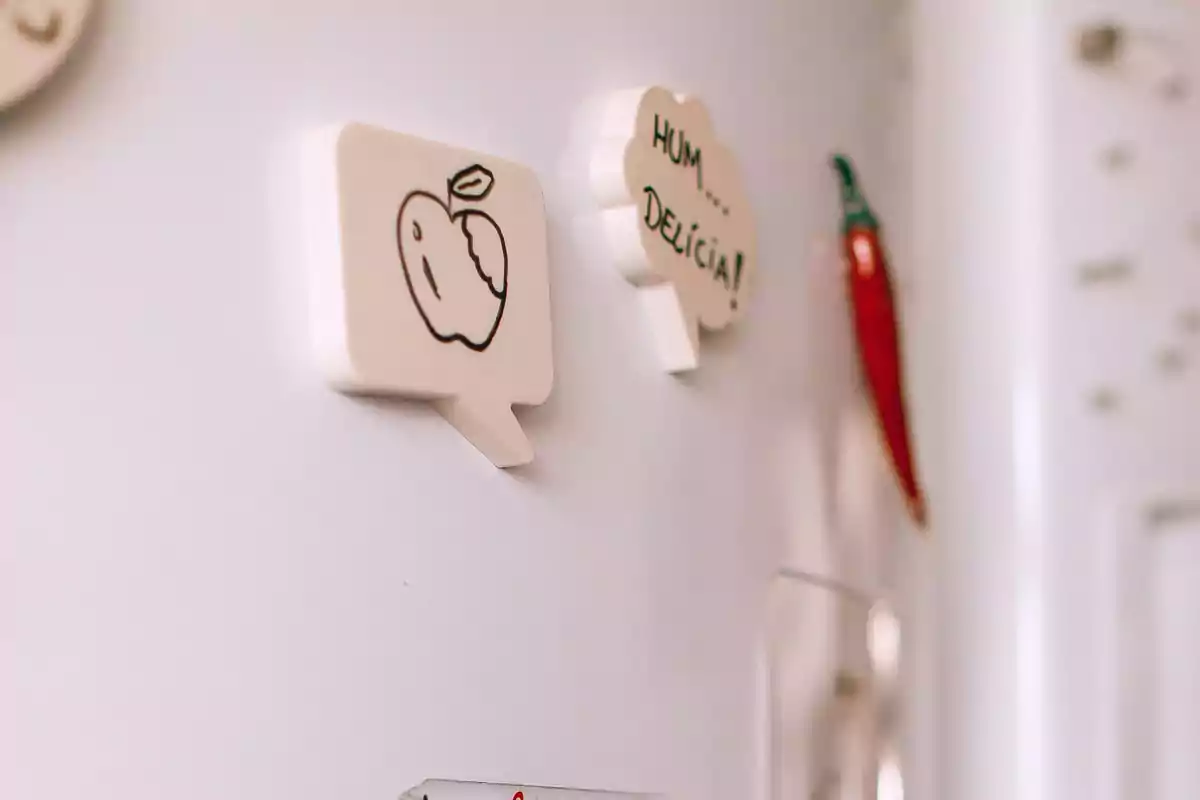 Imanes en forma de bocadillo de cómic en un refrigerador, uno con un dibujo de una manzana y otro con la frase Imanes en forma de bocadillo de cómic en un refrigerador, uno con un dibujo de una manzana y otro con la frase