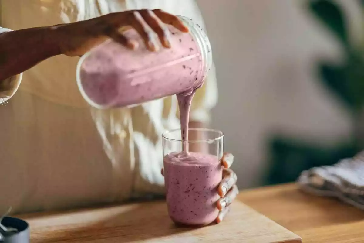 Persona llenando un vaso con un batido de tono rosado