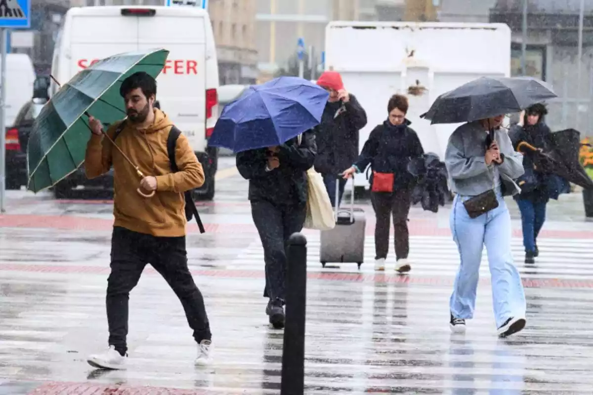 Varias personas cruzando una calle con paraguas en un día de lluvia en Santander